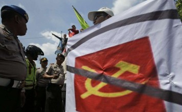 A man carries a banner of defaced communist symbol during a protest against the discussion of anti-communist massacres in 1965-66 outside the venue of the event in Jakarta, Indonesia, Monday, April 18, 2016. Photo: AP