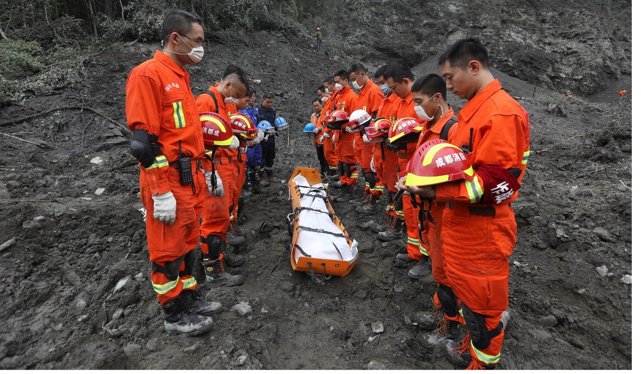 Rescue workers stand in silent tribute before evacuating a body from the landslide site in Xinmo village on Sunday. Photo: Reuters