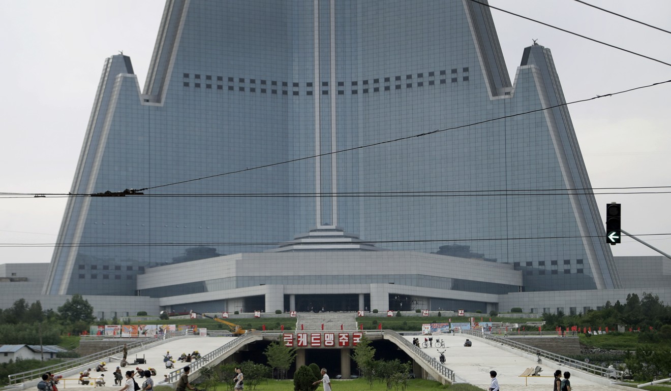 People walk past the 105-storey pyramid shaped Ryugyong Hotel where men are seen working on a driveway leading up into its entrance in Pyongyang. Photo: AP