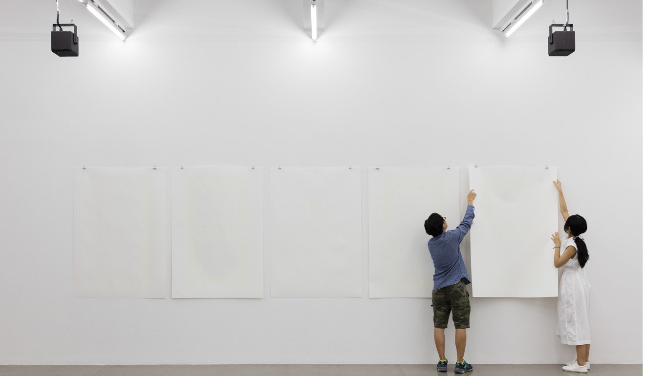 A pair of “dalangs” hang a white sheet on the wall as part of the installation Fade to Black by artist Philippe Parreno.