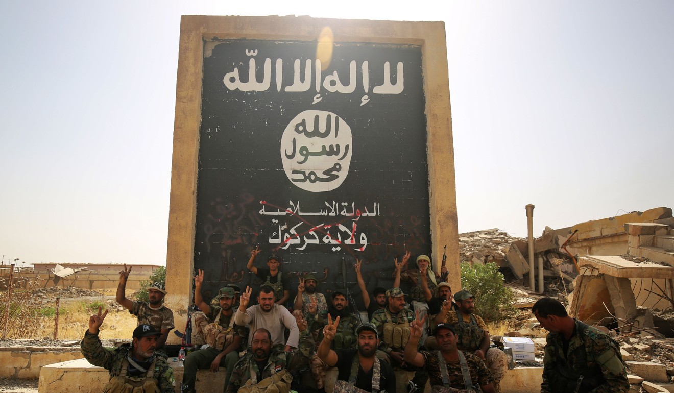 Fighters from the Hashed al-Shaabi (Popular Mobilisation units), backing Iraqi forces, pose in front of a mural depicting the emblem of the Islamic State as troops advance through Hawija onThursday. Photo: AFP