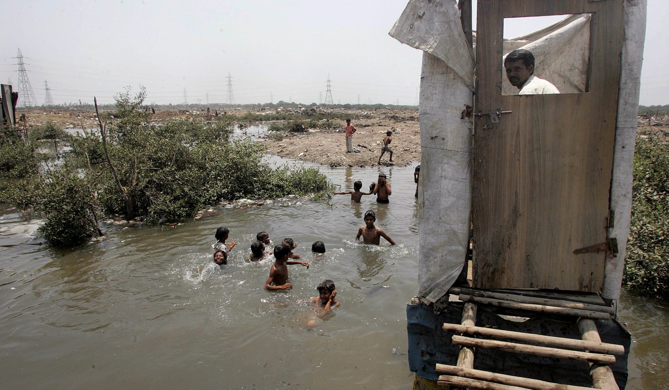 A slum resident uses a toilet that opens into the water below where children are swimming Mankhurd, Mumbai. Photo: AFP