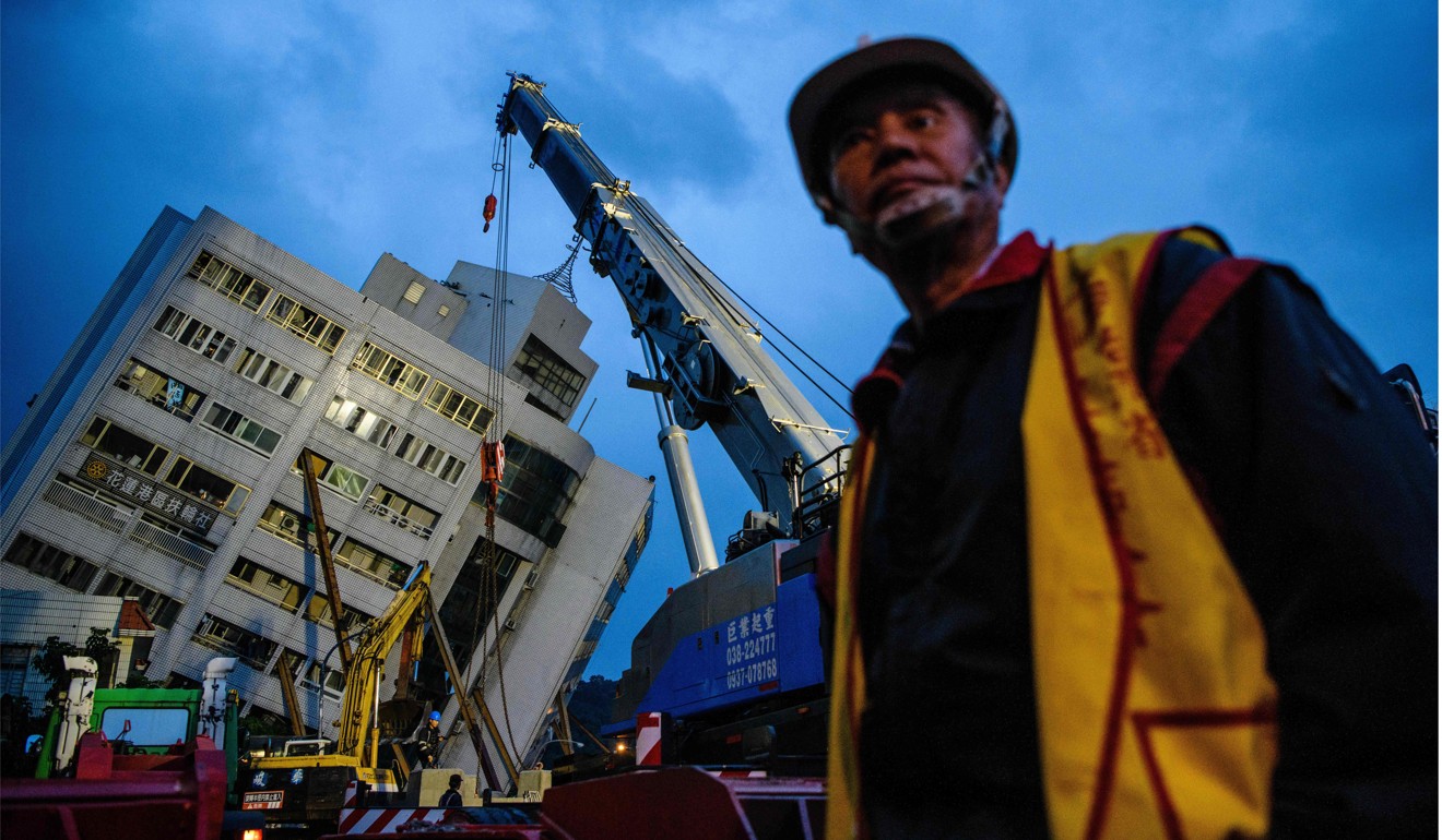 A rescue worker walks past a crane as the Yun Tsui building (back) leans to one sid. Photo: AFP