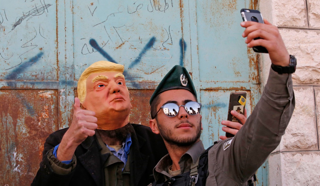 An Israeli soldier takes a selfie with an Israeli settler dressed in a mask of US President Donald Trump in the divided West Bank town of Hebron on Thursday. Photo: Agence France-Presse