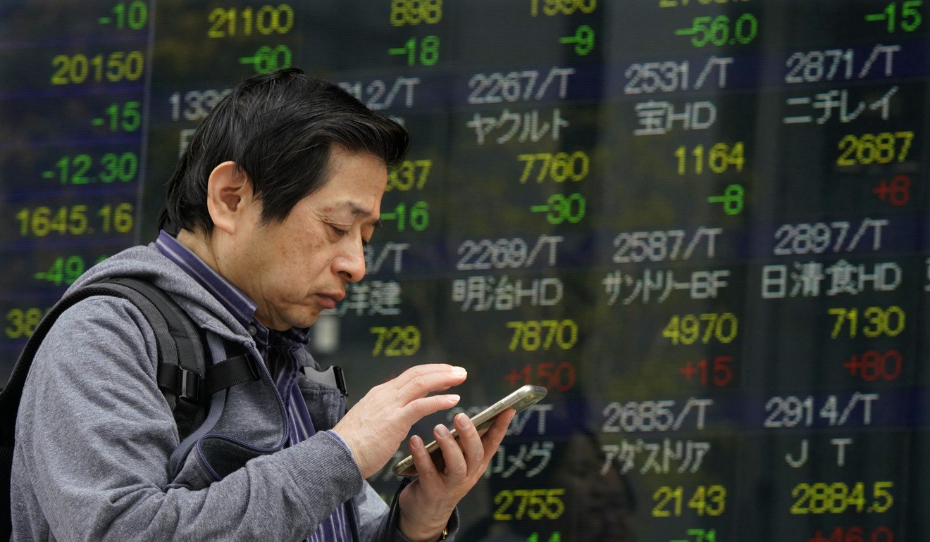 A man uses a smartphone in front of an electronic stock indicator of a securities firm in Tokyo. Japanese investors are attracted to the higher US Treasury yields. Photo: AP 