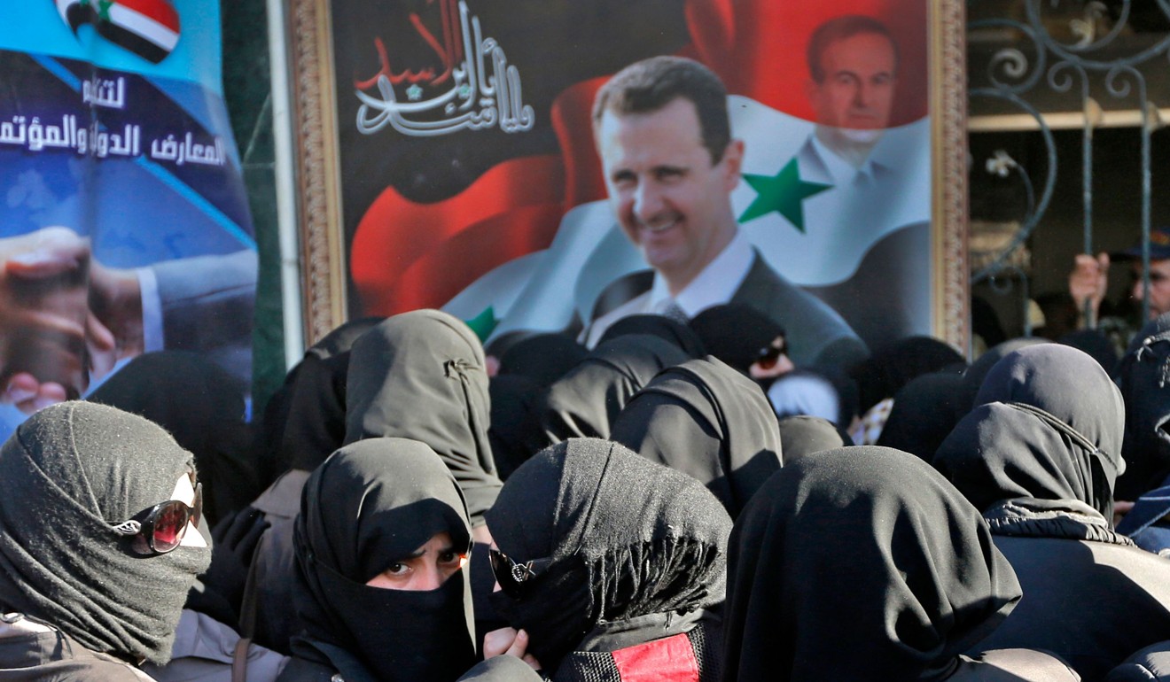 Syrian women walk past a large portrait of President Bashar al-Assad and a watermarked portrait of his late father and former President Hafez al-Assad as they queue to attend the government-sponsored ‘Ghouta Shopping Festival’. Photo: AFP