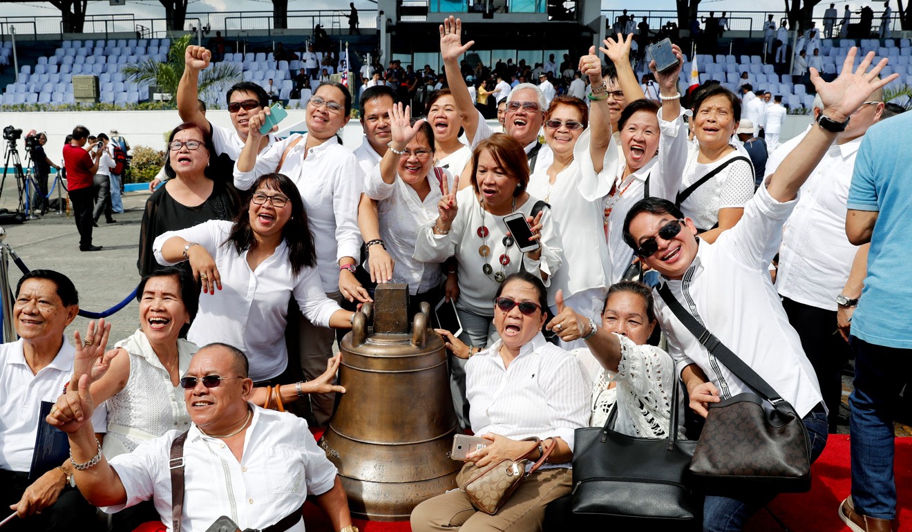 Filipinos pose next to a Balangiga bell after its arrival at Villamor Air Base in Pasay. Photo: Reuters