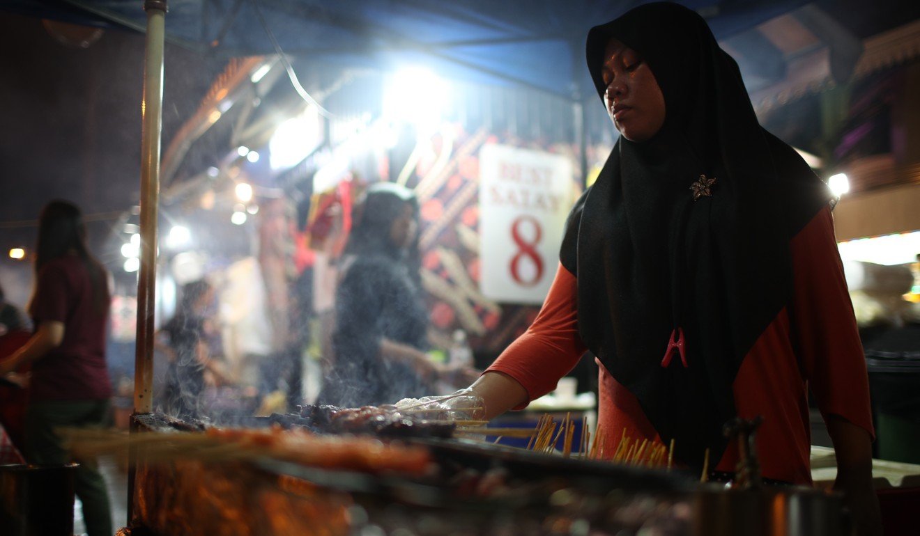 A hawker cooks satay meat skewers at her stall at Lau Pa Sat Food Centre in Singapore. Photo: EPA