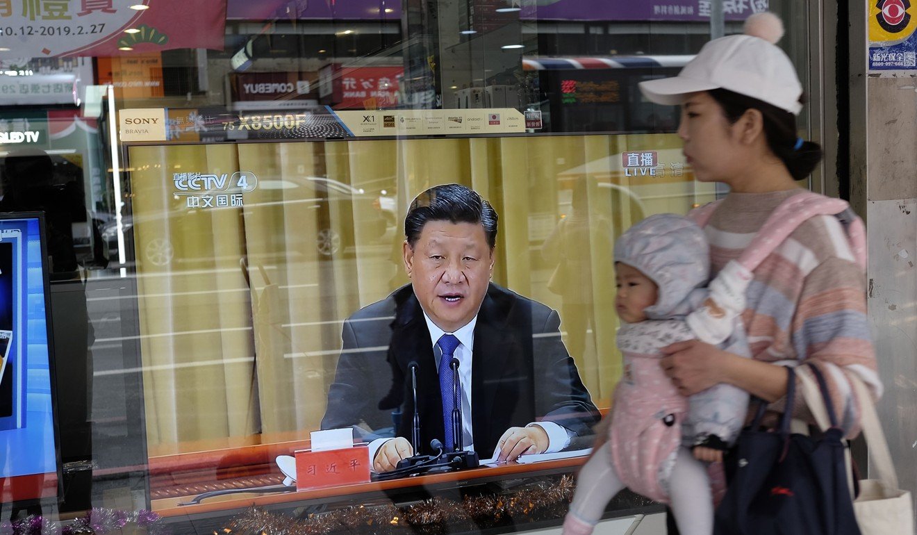 A mother carries her child past a television in New Taipei City showing Xi Jinping’s speech calling for unity. Photo: AFP
