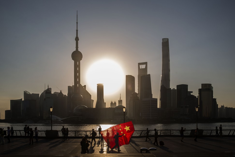 A man carrying a kite in the shape of the Chinese national flag walks along the Bund, while buildings of Pudong's Lujiazui financial district stand across the Huangpu River as the sun rises in Shanghai. Photo: Bloomberg