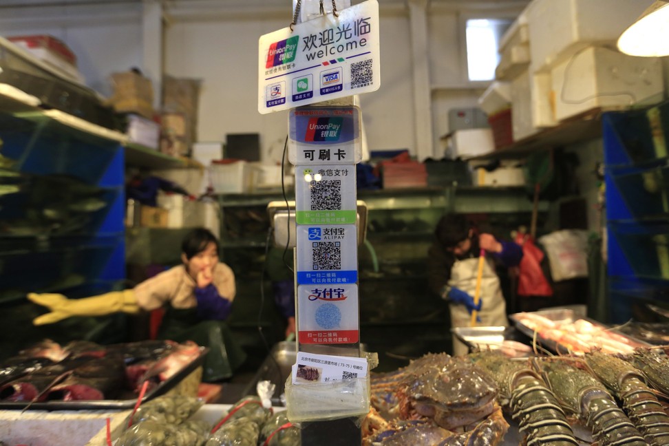 Placards at a seafood stall in a Beijing market show how vendors are adapting to cashless payments by accepting UnionPay cards, along with QR codes for WeChat and Alipay. Photo: EPA