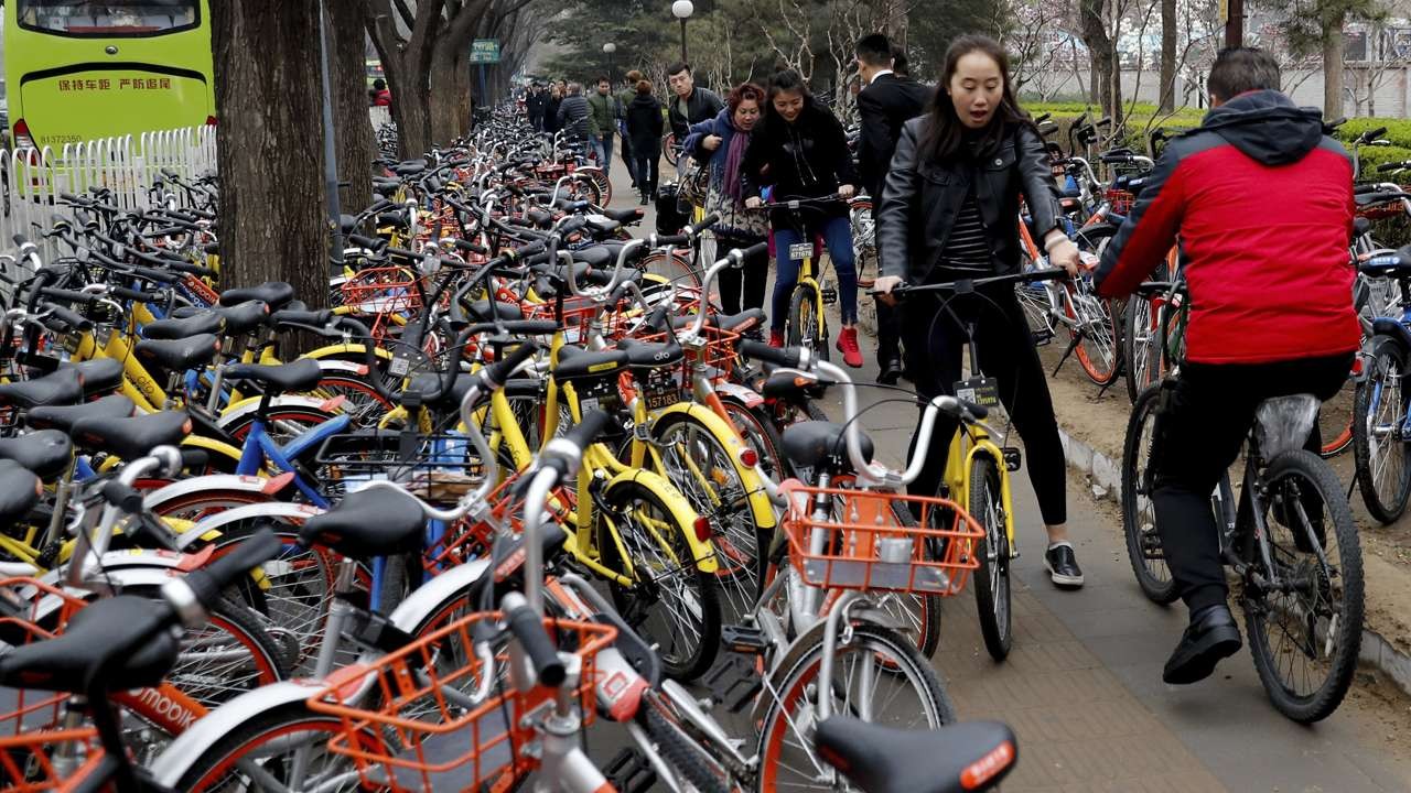 People riding Ofo’s yellow bicycles try to pedal along a pavement crowded with bicycles from various bike-sharing companies in Beijing last month. (Picture: South China Morning Post)