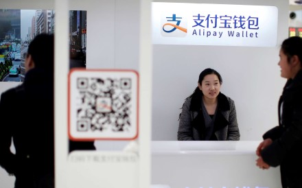 A sales assistant sits behind and under Alipay logos at a train station in Shanghai on February 9, 2015. Photo: Reuters