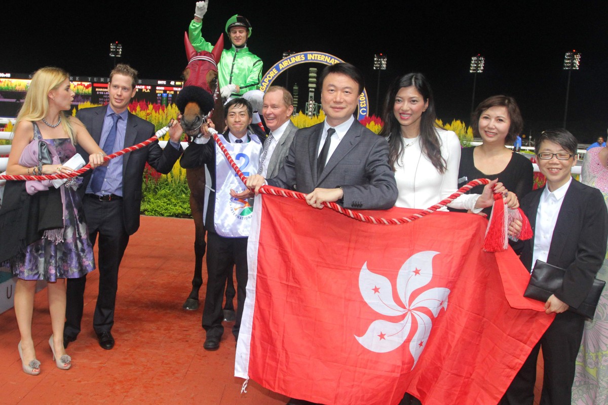 Owner Steven Lo Kit-sing holds the Bauhinia flag, with trainer John Moore behind him, after Military Attack laid siege to Kranji last night. Photo: Kenneth Chan