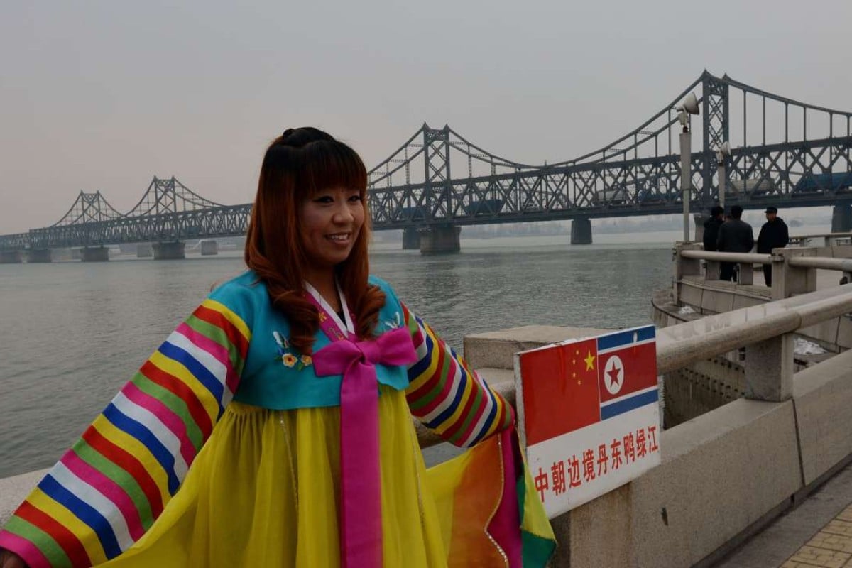 A Chinese woman poses in Korean clothing as trucks carrying Chinese-made goods cross into North Korea on the Sino-Korean Friendship Bridge at the border town of Dandong. Chinese tourism to North Korea is on the increase. Photo: AFP